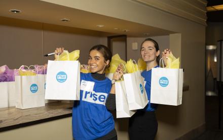 Two women smiling in Rise shirts holding gift bags