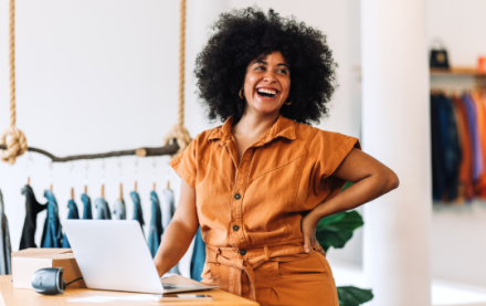 Black woman smiling, standing next to her computer in her clothing boutique