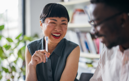 Asia woman holding a pen smiles as she speaks to a colleague
