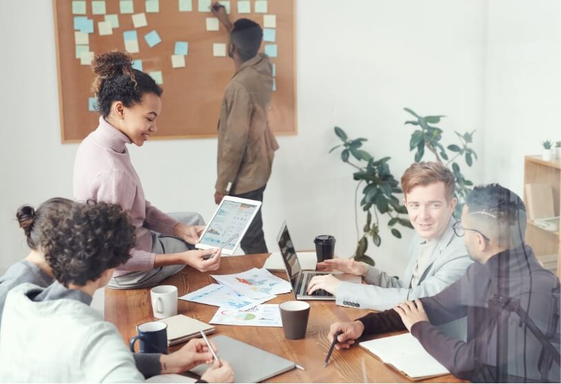 A photo of a diverse group of colleagues working together, arranging Post-It notes on a corkboard.