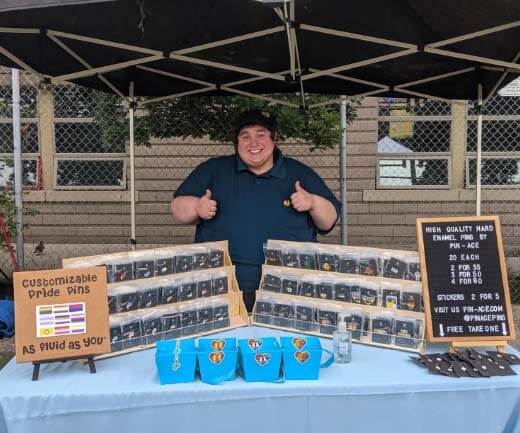 Darcy Alemany, posing with two thumbs up in front of a display of his products.