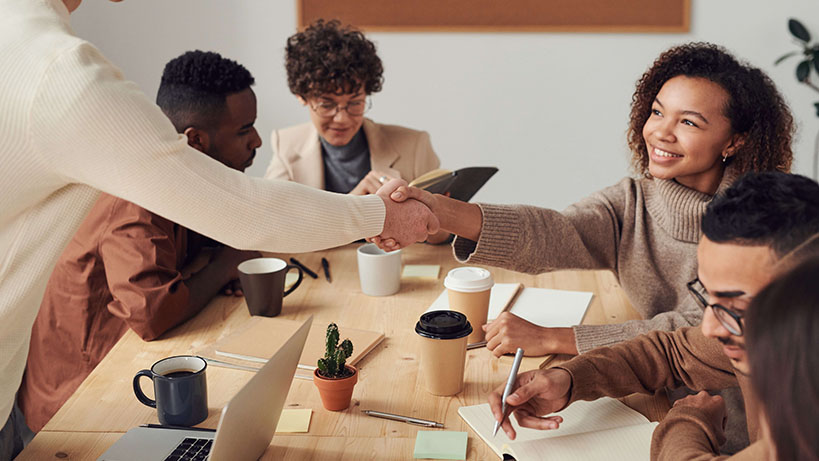 A photo of a diverse group of colleagues, with two reaching out to shake hands.