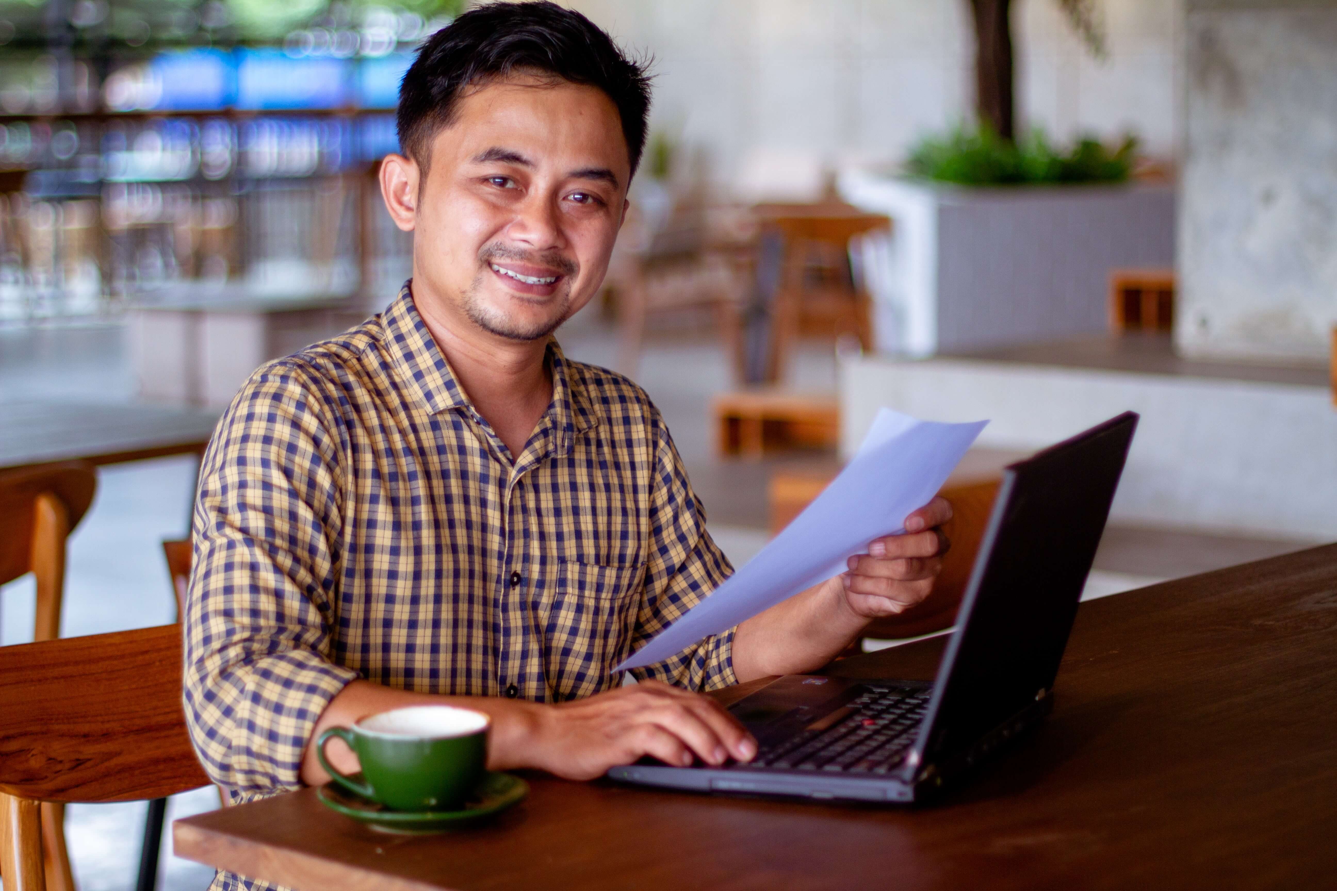 A photo of a man in a coffee shop, working on a laptop.